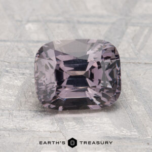 A 2.04-carat, cushion-cut purple spinel is displayed on a textured gray surface with “Earth’s Treasury” at the bottom.