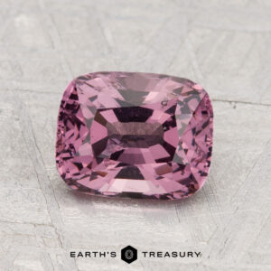 A 2.04-carat cushion-cut pink spinel is displayed on a textured gray surface with "EARTH'S TREASURY" text at the bottom.