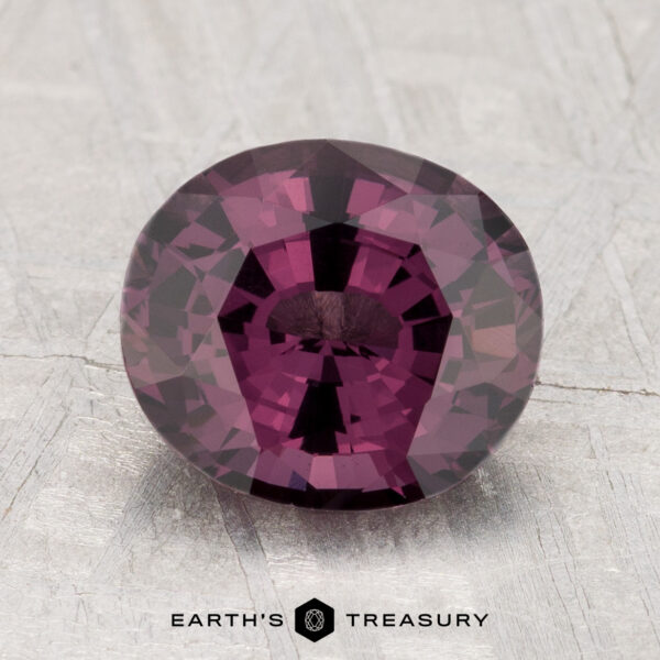 2.63-Carat Spinel A 2.63-carat round faceted purple spinel is displayed on a light textured surface with "EARTH'S TREASURY" written below.