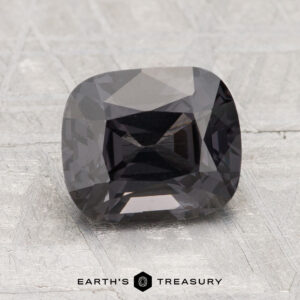 A 2.45-carat cushion-cut gray spinel with a faceted surface is displayed on a textured gray background. The text "Earth's Treasury" appears at the bottom.