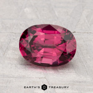 A 2.09-carat faceted oval pink spinel is displayed on a textured light gray surface, with "EARTH'S TREASURY" text and logo beneath.