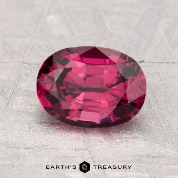 2.09-Carat Spinel A 2.09-carat faceted oval pink spinel is displayed on a textured light gray surface, with "EARTH'S TREASURY" text and logo beneath.