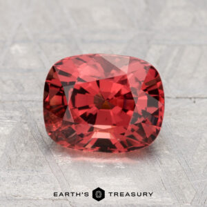A 2.12-carat cushion-cut Spinel rests on a textured gray surface, with "EARTH'S TREASURY" displayed at the bottom of the image.