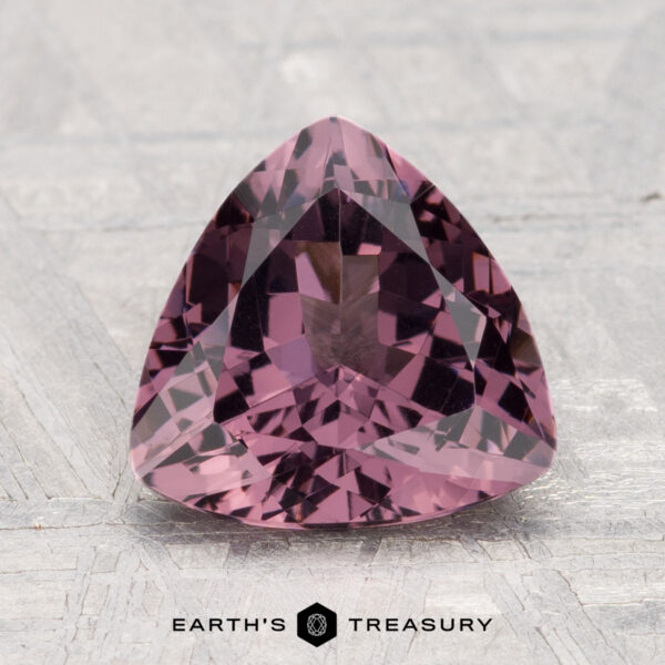 2.52-Carat Spinel A 2.52-carat, faceted triangular purple spinel is showcased on a flat, textured surface with "Earth's Treasury" written below.