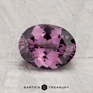A 2.02-carat oval-cut faceted purple spinel rests on a textured light gray surface, with the text "EARTH'S TREASURY" at the bottom.