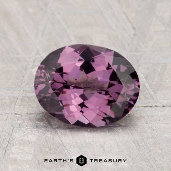 2.02-Carat Spinel A 2.02-carat oval-cut faceted purple spinel rests on a textured light gray surface, with the text "EARTH'S TREASURY" at the bottom.