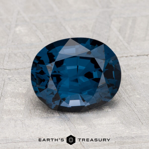 2.00-Carat Spinel A 2.00-carat, deep blue oval-cut spinel is displayed on a textured light gray surface with the text "EARTH'S TREASURY" beneath it.