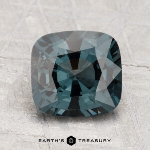 A 2.54-carat spinel gemstone is displayed on a textured light gray surface with the "Earth's Treasury" logo below.