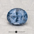 A 2.04-carat oval-cut blue spinel with multiple facets rests on a textured light gray surface. The text "EARTH'S TREASURY" appears at the bottom.