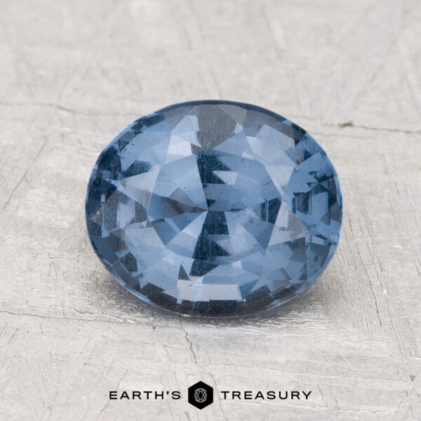 2.04-Carat Spinel A 2.04-carat oval-cut blue spinel with multiple facets rests on a textured light gray surface. The text "EARTH'S TREASURY" appears at the bottom.
