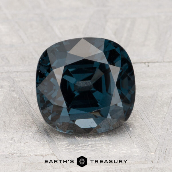 2.80-Carat Spinel A 2.80-carat cushion-cut dark blue spinel is shown on a light gray textured surface, with the "Earth's Treasury" logo and text at the bottom.
