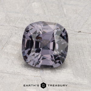 A 1.60-carat, cushion-cut violet-gray spinel is shown on a light textured surface with "Earth's Treasury" displayed underneath.