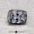 A 1.63-carat cushion-cut dark gray Spinel is shown on a textured light gray surface with "EARTH'S TREASURY" text at the bottom.