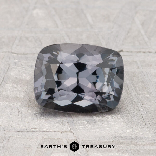 1.63-Carat Spinel A 1.63-carat cushion-cut dark gray Spinel is shown on a textured light gray surface with "EARTH'S TREASURY" text at the bottom.