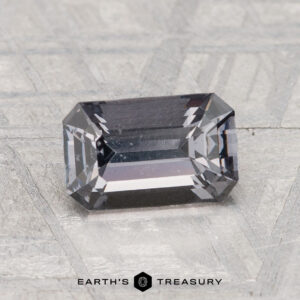 A 1.50-carat spinel with beveled edges rests on a textured surface, featuring "Earth's Treasury" and a hexagonal logo below.