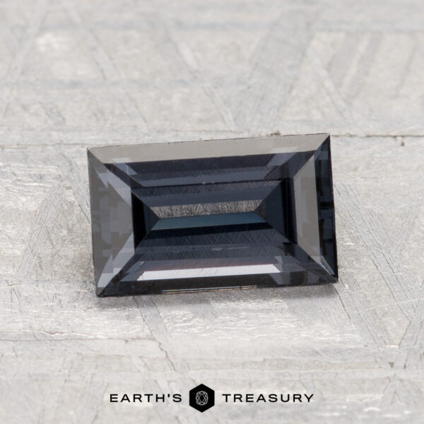 1.53-Carat Spinel A 1.53-carat, dark blue rectangular step-cut spinel is displayed on a textured light gray surface with "EARTH'S TREASURY" text at the bottom.