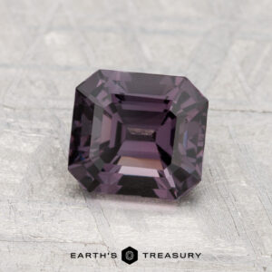 A 1.53-carat, square-cut deep purple Spinel displayed on a textured light grey surface with "EARTH'S TREASURY" at the bottom.