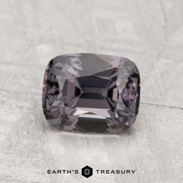 1.64-Carat Spinel A 1.64-carat faceted rectangular Spinel with a dark, muted purple hue is displayed on a light, textured surface; the "Earth's Treasury" logo appears at the bottom.