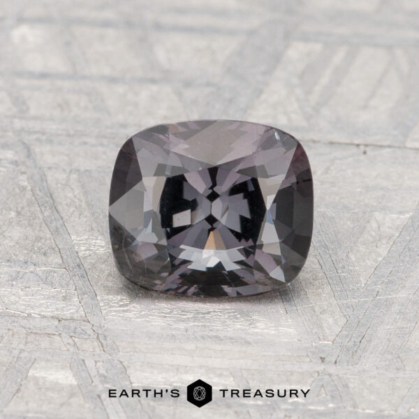 1.30-Carat Spinel A 1.30-carat cushion-cut spinel in dark gray rests on a textured light gray surface, with "EARTH'S TREASURY" inscribed at the bottom.