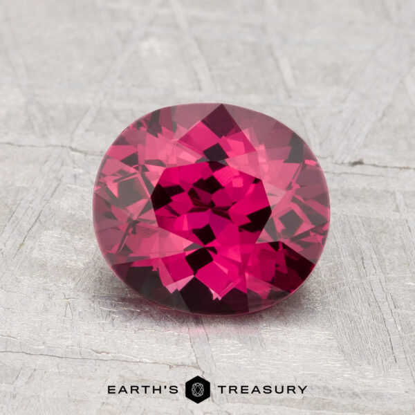 1.76-Carat Spinel A 1.76-carat round, faceted deep pink spinel is displayed on a textured gray surface with the text "EARTH'S TREASURY" below.