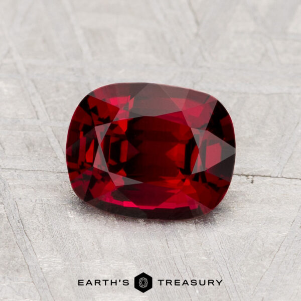 1.36-Carat Spinel A cushion-cut 1.36-carat Spinel gemstone is displayed on a textured light gray surface, with the text "EARTH'S TREASURY" underneath.