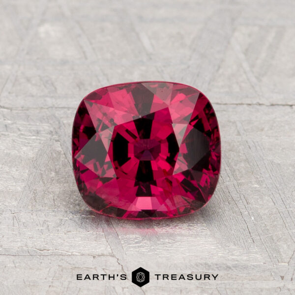 1.61-Carat Spinel A 1.61-carat cushion-cut red Spinel is displayed on a light gray textured surface with "EARTH'S TREASURY" below.