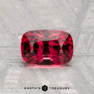 A 1.62-carat cushion-cut, deep red Spinel is displayed on a light, textured background with the "EARTH'S TREASURY" logo beneath.