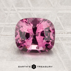 A 1.94-carat cushion-cut deep pink spinel is displayed on a textured, light surface with "EARTH'S TREASURY" at the bottom.
