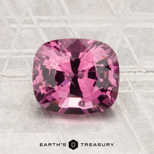 1.94-Carat Spinel A 1.94-carat cushion-cut deep pink spinel is displayed on a textured, light surface with "EARTH'S TREASURY" at the bottom.