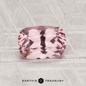 A 1.24-carat cushion-cut pink Spinel is displayed on a patterned gray surface, with the text "EARTH'S TREASURY" at the bottom of the image.