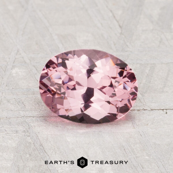 1.36-Carat Spinel A 1.36-carat faceted oval pink spinel is displayed on a light gray textured surface with the text "EARTH'S TREASURY" below it.