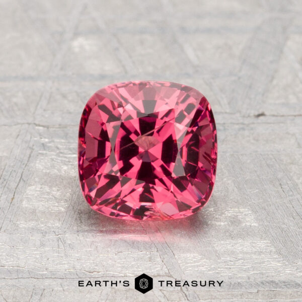 1.26-Carat Spinel A 1.26-carat cushion-cut reddish-pink spinel is displayed on a textured gray surface, with "Earth's Treasury" visible at the bottom.