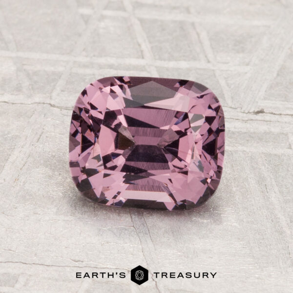 1.49-Carat Spinel A 1.49-carat cushion-cut purple Spinel is displayed on a textured, light gray surface with the text "EARTH'S TREASURY" below.
