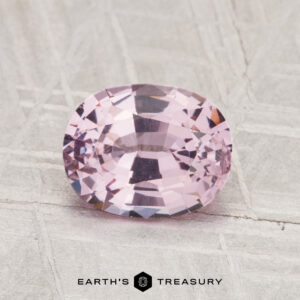 A 1.42-carat, faceted oval-cut pink spinel is displayed on a textured light gray surface with the "Earth's Treasury" logo at the bottom.