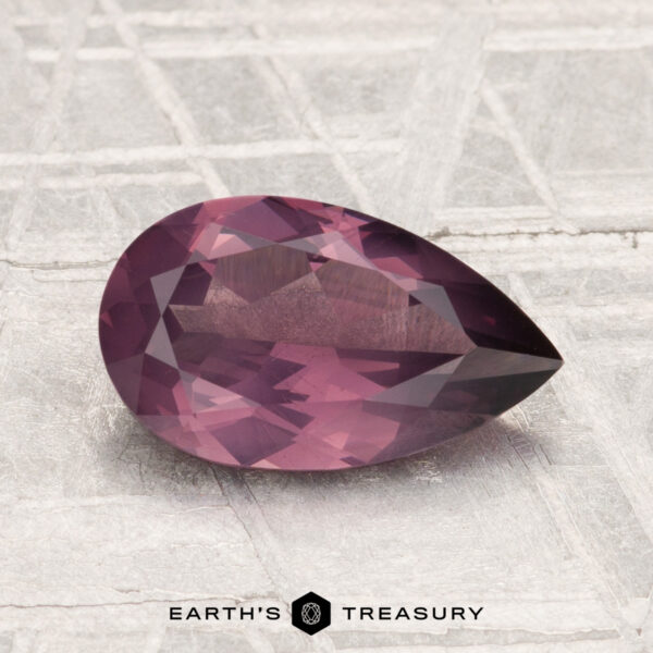 1.56-Carat Spinel A faceted, pear-shaped 1.56-carat spinel gemstone is displayed on a textured light-gray surface with "Earth's Treasury" branding at the bottom.