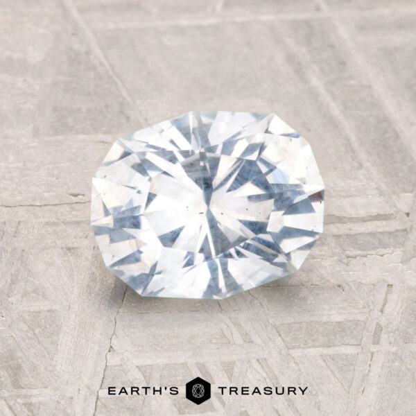 1.78-Carat Montana Sapphire A 1.78-carat, round brilliant-cut Montana Sapphire is displayed on a textured gray surface, with the text "EARTH'S TREASURY" beneath it.