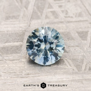 The 0.84-Carat Montana Sapphire is shown on a textured gray metallic surface with "EARTH'S TREASURY" at the bottom.