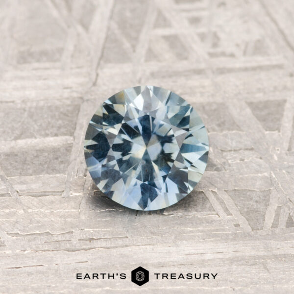 0.84-Carat Montana Sapphire The 0.84-Carat Montana Sapphire is shown on a textured gray metallic surface with "EARTH'S TREASURY" at the bottom.