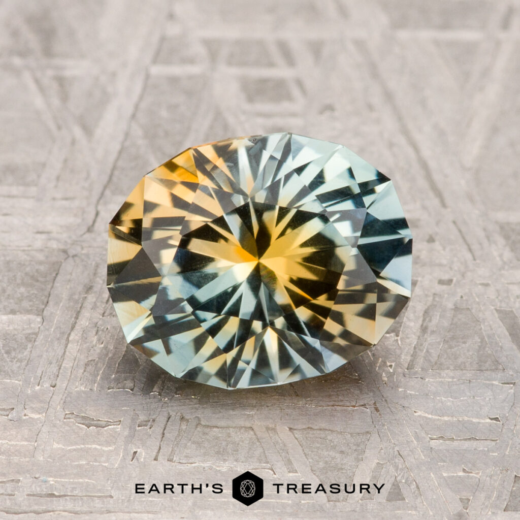 A 2.00-carat Montana sapphire with yellow and gray hues rests on a textured surface, with the "EARTH'S TREASURY" text and logo displayed below.