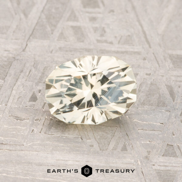 1.14-Carat Montana Sapphire A 1.14-carat faceted oval pale yellow Montana sapphire is displayed on a textured gray surface with the text "EARTH'S TREASURY" at the bottom.