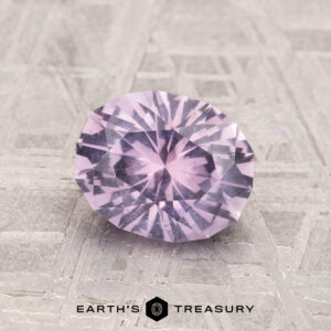 The 1.53-Carat Lilac Pink Montana Sapphire, oval-cut and faceted, is displayed on a textured light gray surface with the Earth’s Treasury logo below.
