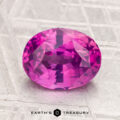 A 3.04-carat, oval-cut sapphire in vivid pink sits on a light-patterned surface with the "EARTH'S TREASURY" text below.