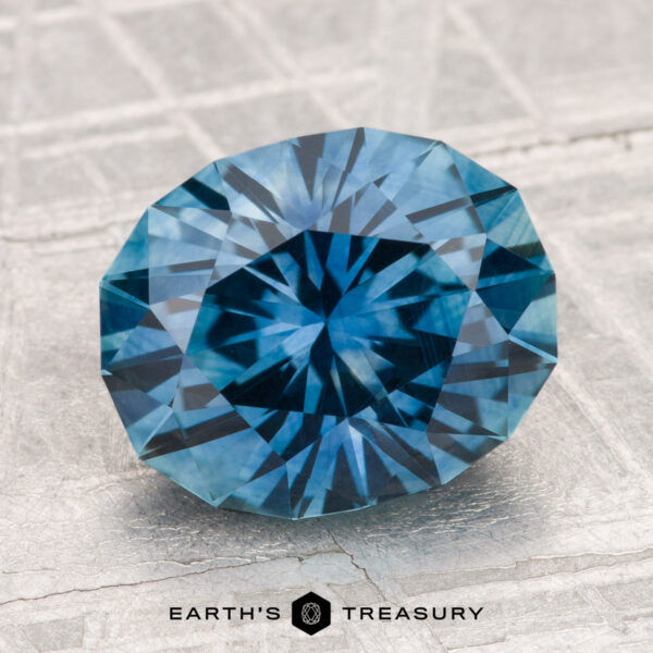 3.74-Carat Montana Sapphire (Heated) A faceted 3.74-carat heated Montana sapphire with a starburst pattern sits on a textured, light surface. "EARTH'S TREASURY" is displayed at the bottom.