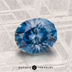 A 2.08-carat heated Montana sapphire is showcased on a textured, light surface with "EARTH'S TREASURY" displayed below.