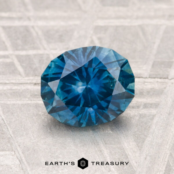 1.59-Carat Montana Sapphire (Heated) A 1.59-carat heated Montana sapphire with an oval cut is displayed on a textured gray surface, with "EARTH'S TREASURY" shown below the gemstone.
