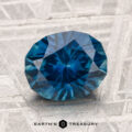 A faceted round blue 2.85-carat Montana Sapphire (Heated) rests on a textured gray surface, with the text “Earth’s Treasury” at the bottom.