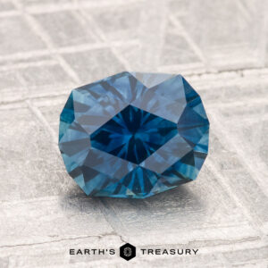 A 2.09-carat heated Montana sapphire is displayed on a textured, light-colored surface with "EARTH'S TREASURY" below.