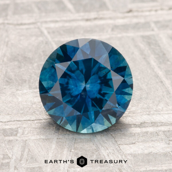 1.74-Carat Montana Sapphire (Heated) A 1.74-carat heated Montana sapphire, round brilliant-cut, stands upright on a textured surface with "EARTH'S TREASURY" below.