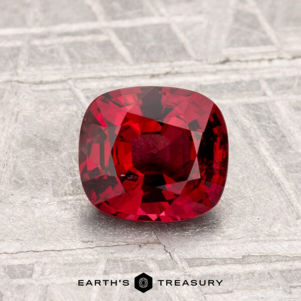 1.31-Carat Spinel A 1.31-carat cushion-cut Spinel is displayed on a textured, silver-toned surface with "Earth's Treasury" written at the bottom.