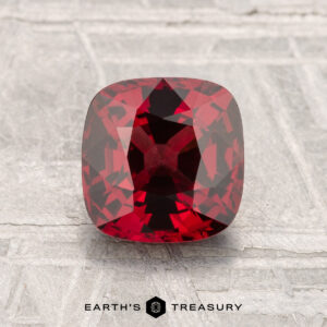 A 1.67-carat cushion-cut spinel is shown on a light gray textured surface with the text "Earth's Treasury" below.